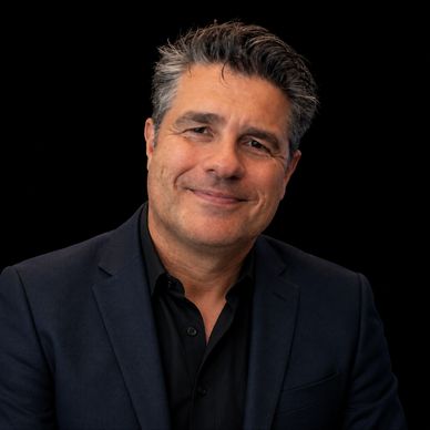Smiling man in a dark suit against a black background.