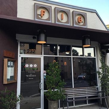 Front entrance of FIG restaurant with glass doors and a bench outside.