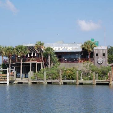 Waterfront restaurant with palm trees and a clear sky.