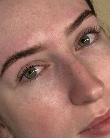 Close-up of a face with green eyes, natural skin texture, and well-groomed eyebrows.