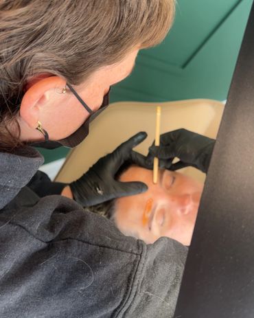 A person getting their eyebrows shaped by a professional wearing gloves.