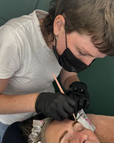 A beautician carefully applies eyebrow makeup to a client wearing a headband.