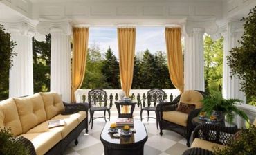 Elegant outdoor seating area with beige sofas and black chairs under white pillars.