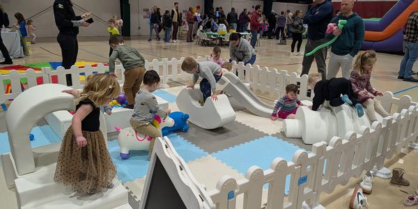 Children playing on soft playground equipment inside a fenced area.