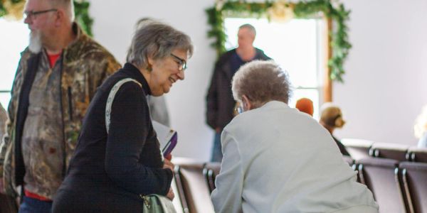 Two elderly women engaged in conversation inside a room.