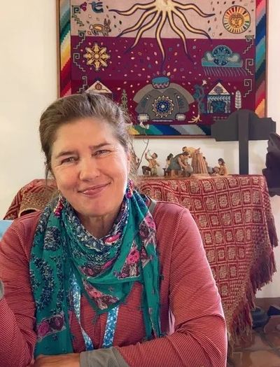 Smiling woman wearing a colorful scarf and red top, sitting indoors.