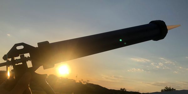A caulking gun held against a sunset background outdoors.