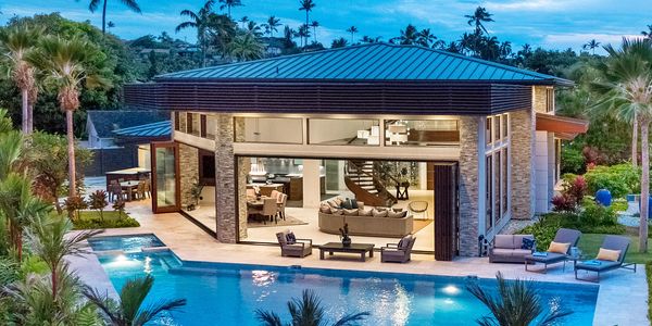 Modern house with large windows and a pool surrounded by tropical plants.