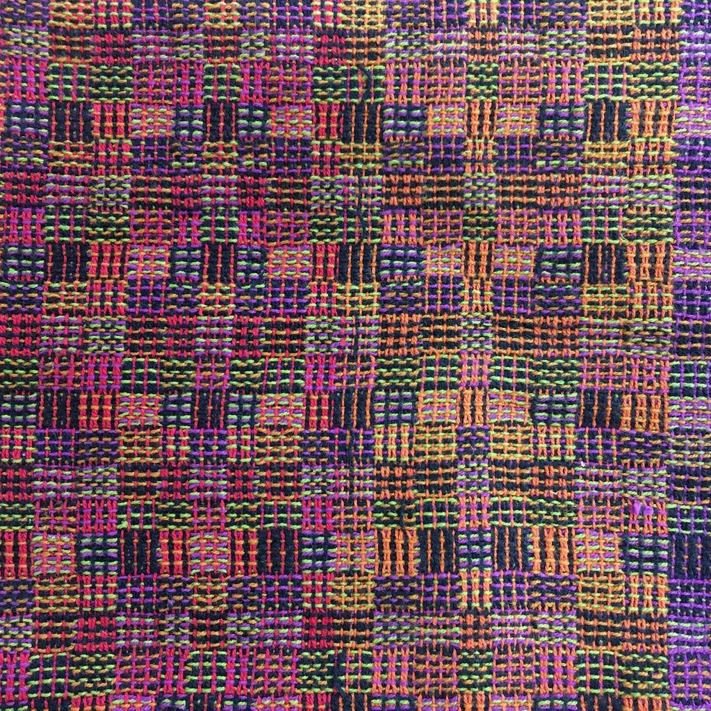 Close up of handwoven cloth in small checks of multi-colured mini stripes in shades of orange, pink,
