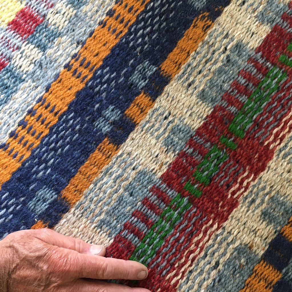 Close up of a hand woven wool rug in multi coloured stripes of blue, orange, beige, red and green, w
