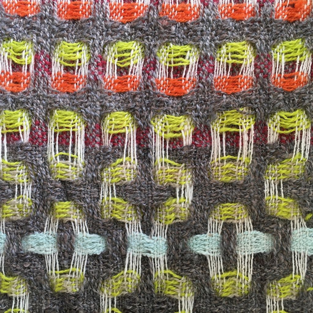 Close up of handwoven woollen scarf in grey, white, orange, lime and pale blue.