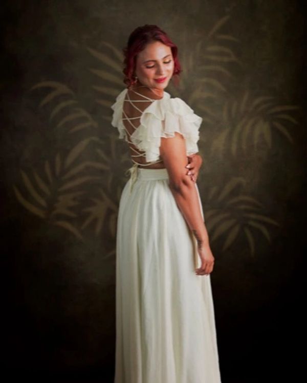 Woman in elegant white dress with ruffled sleeves and open back, posing gracefully.
