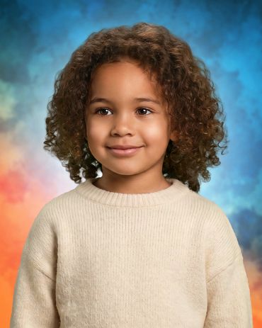 A young child with curly hair wearing a cream sweater smiles gently.