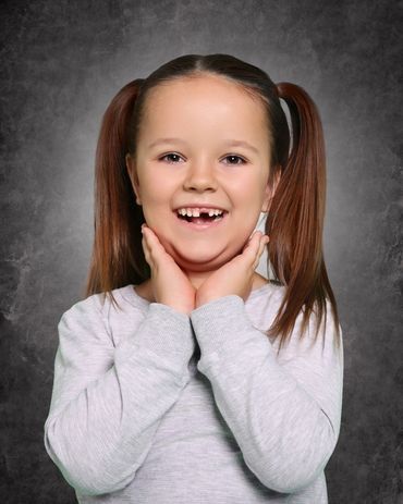 Happy girl with pigtails smiling joyfully against a dark background.
