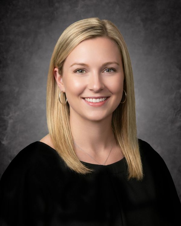 Professional headshot of a smiling woman with blonde hair and hoop earrings.