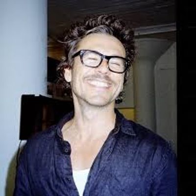 Smiling man wearing glasses and a dark shirt.