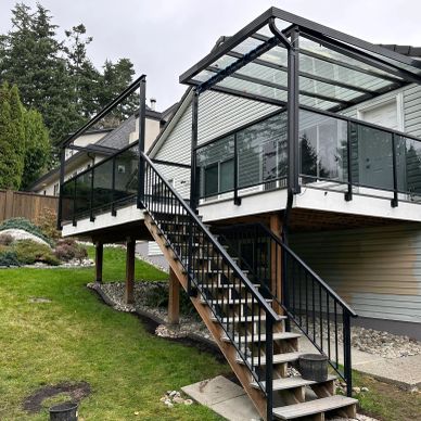 Staircase leading to a covered outdoor deck with glass panel and solid railings.
