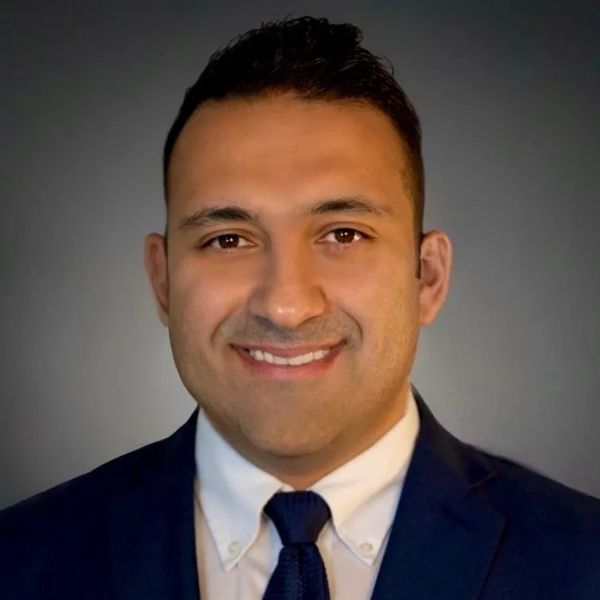 Professional headshot of a man in a suit and tie with a warm smile.