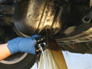 A person draining used motor oil from a vehicle's engine.