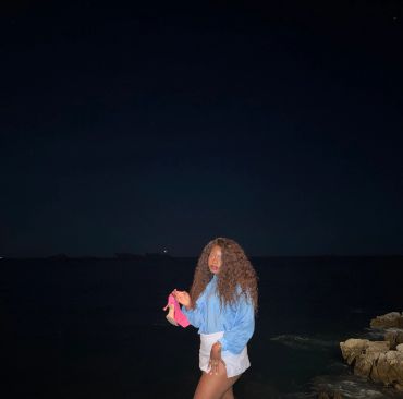 Woman standing near rocks by the dark sea at night.
