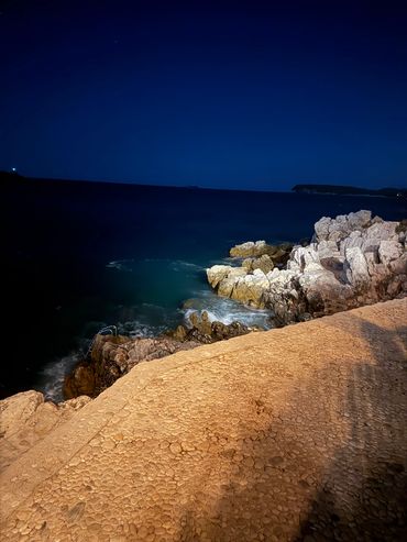 Nighttime rocky shoreline under dark blue sky.