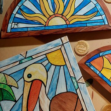 Faux stained glass paintings arranged on the table showing small bits of 3 artworks. Pelican and sun
