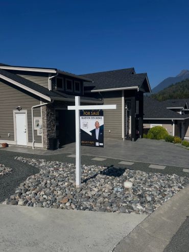 Modern house with a for sale sign in front under clear blue sky.