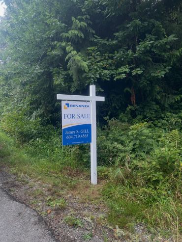 For sale sign in a green, wooded area.