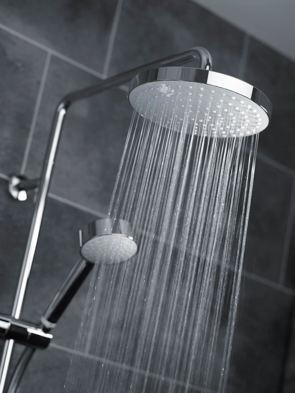 Modern chrome showerhead releasing water in a tiled bathroom.