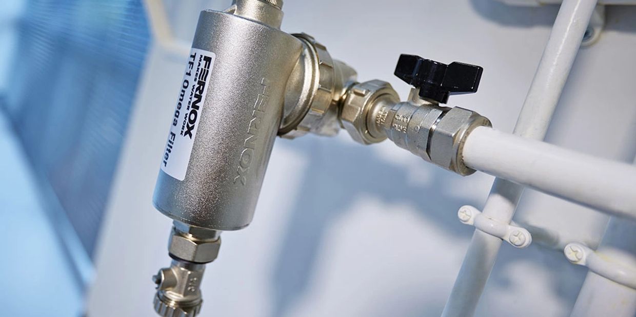 Close-up of a Fernox TF1 Omega Filter installed on white plumbing pipes.