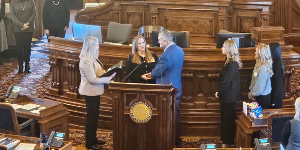 People standing around a podium in a formal setting, possibly a government chamber.