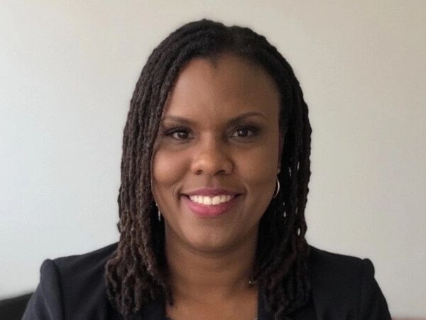 Professional woman with dreadlocks smiling, wearing a blazer and patterned blouse.