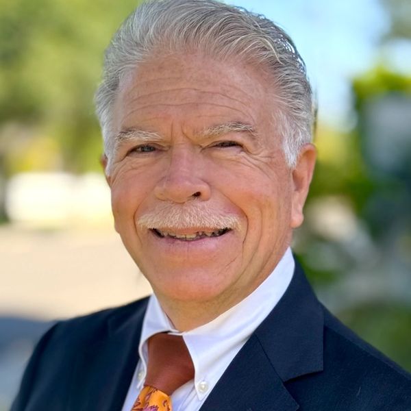 Smiling elderly man in a suit with a colorful tie outdoors.