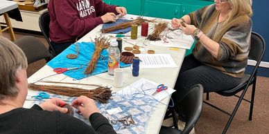 Women sitting at a table making woven baskets.