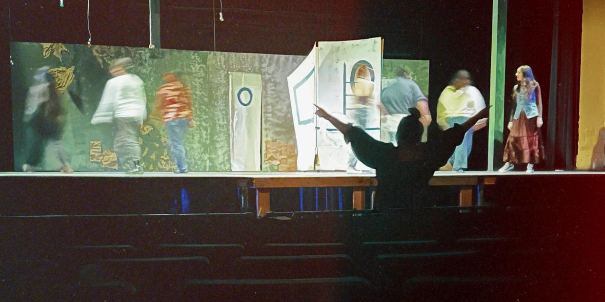 Actors rehearsing on stage with a director guiding from the audience.