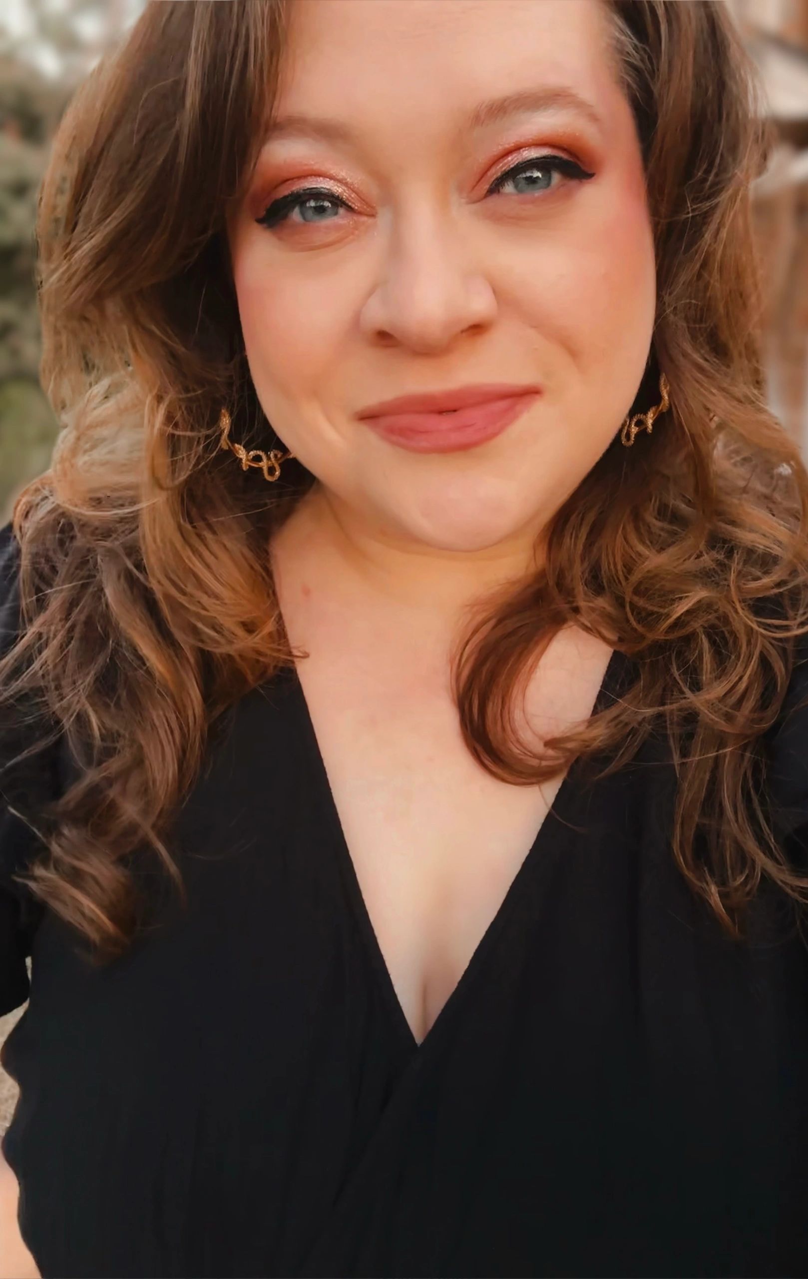 Smiling woman with curled hair wearing a black top and gold earrings.