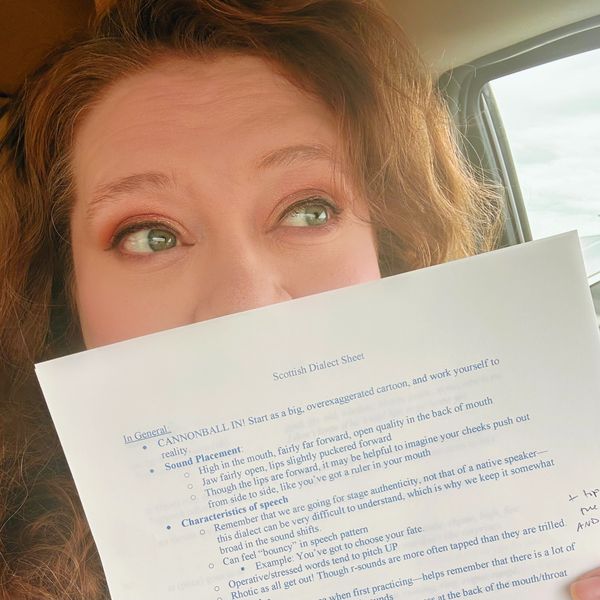 Person holding a Scottish Dialect Sheet inside a car, looking to the side.