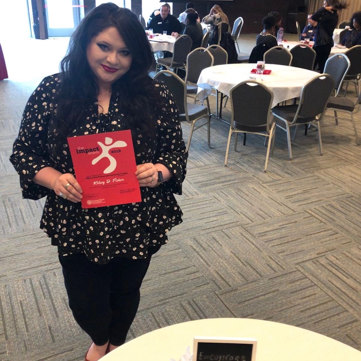 Woman proudly holding an Impact Award certificate at an event.