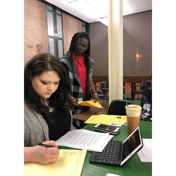 Two women working together with documents and a tablet at a table.
