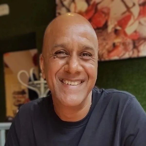 Smiling bald man in a black shirt sitting indoors.
