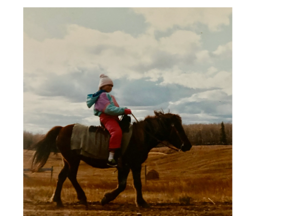 Young girl riding a Shetland pony through a pasture.
