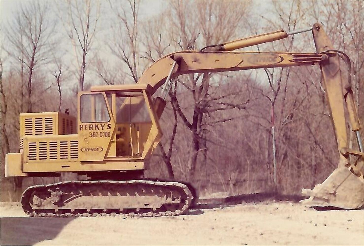 Yellow excavator parked on dirt near leafless trees.