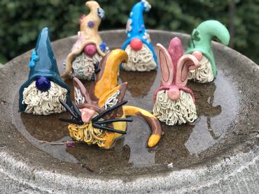 Colorful gnome and bunny figurines arranged in a shallow dish outdoors.