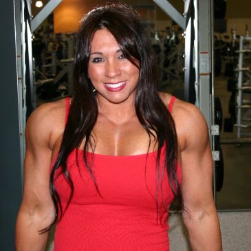 A muscular woman in a red tank top smiling at the gym.