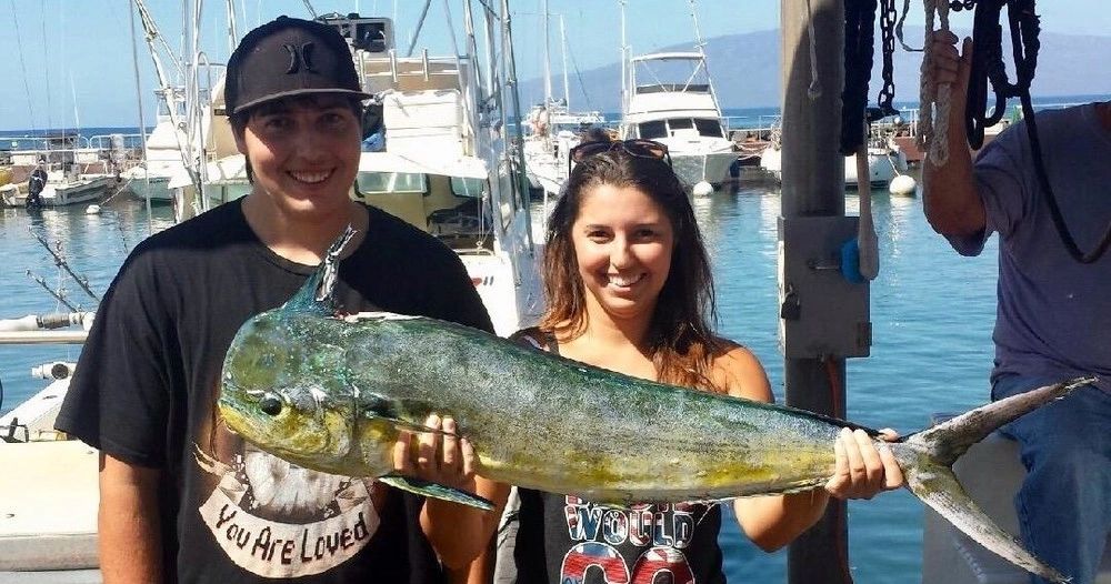 Two people proudly holding a large fish at a marina.