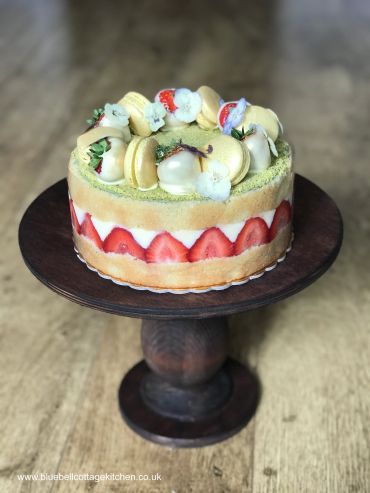 Strawberry layered cake with macarons and white chocolate on wooden stand.