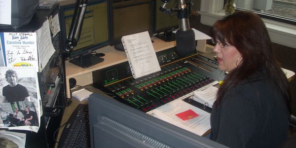 Woman speaking into a microphone in a radio station studio.