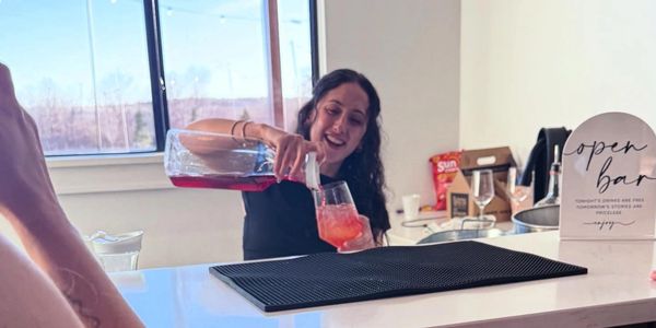 A woman happily pouring a colorful drink at an open bar counter.