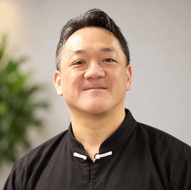 Smiling man in black traditional shirt.