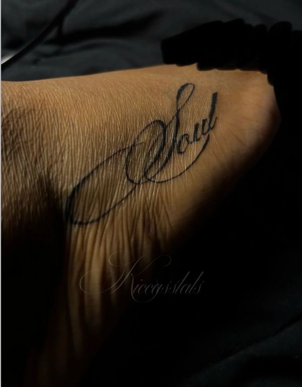 Elegant cursive tattoo on wrist reading 'Loved'.